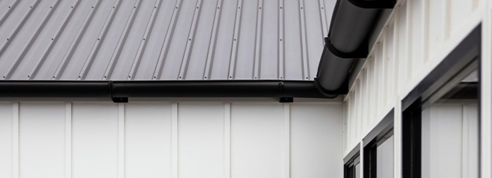 Modern home with black gutters and steel roofing, featuring white panel walls and a seamless gutter system.