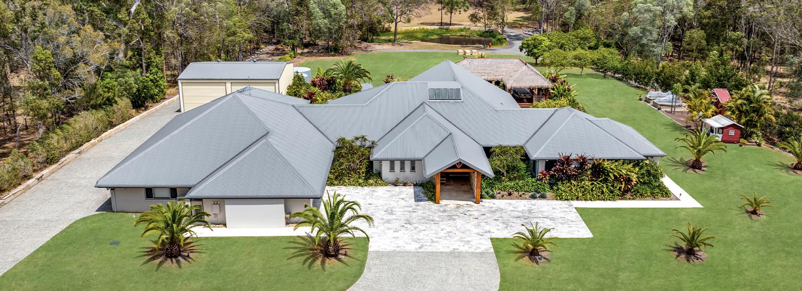 Image Alt Tag: Expansive rural property with multiple rooflines in COLORBOND® steel Basalt®, surrounded by lush greenery.