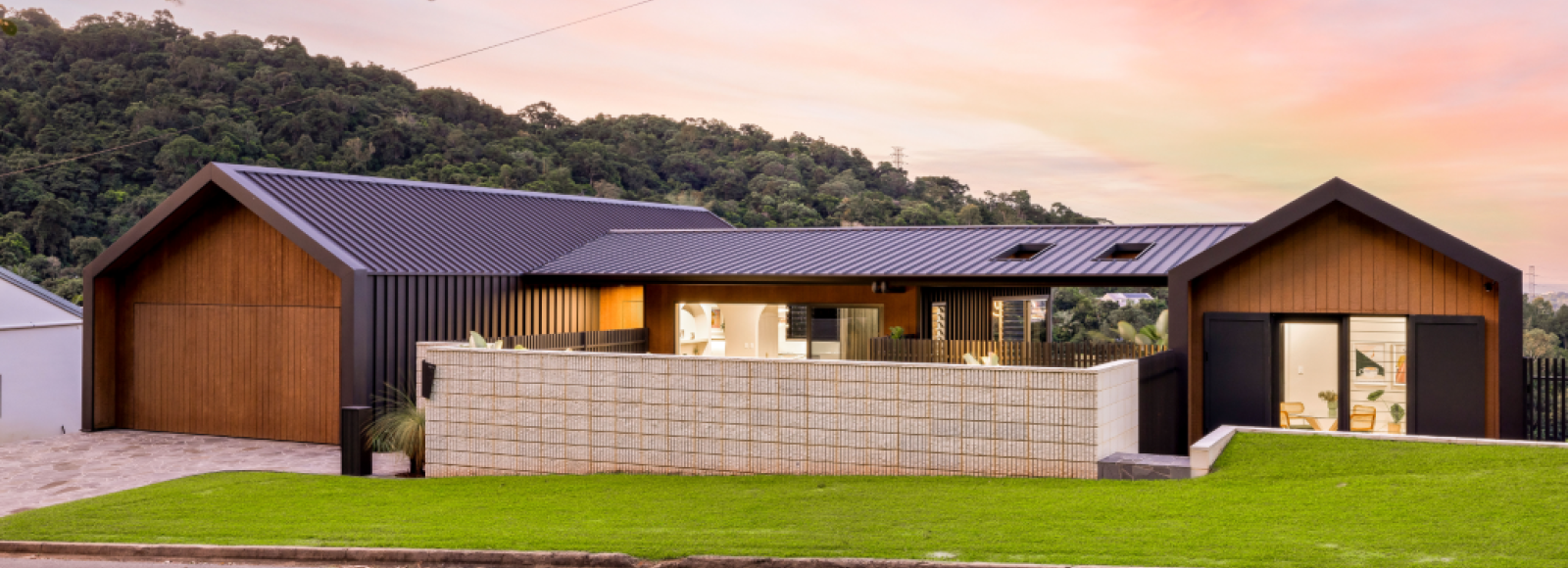 Modern house exterior featuring LYSAGHT® ZENITH® range ENSEAM® cladding in a sleek, dark finish, combined with warm timber paneling and natural stone elements.