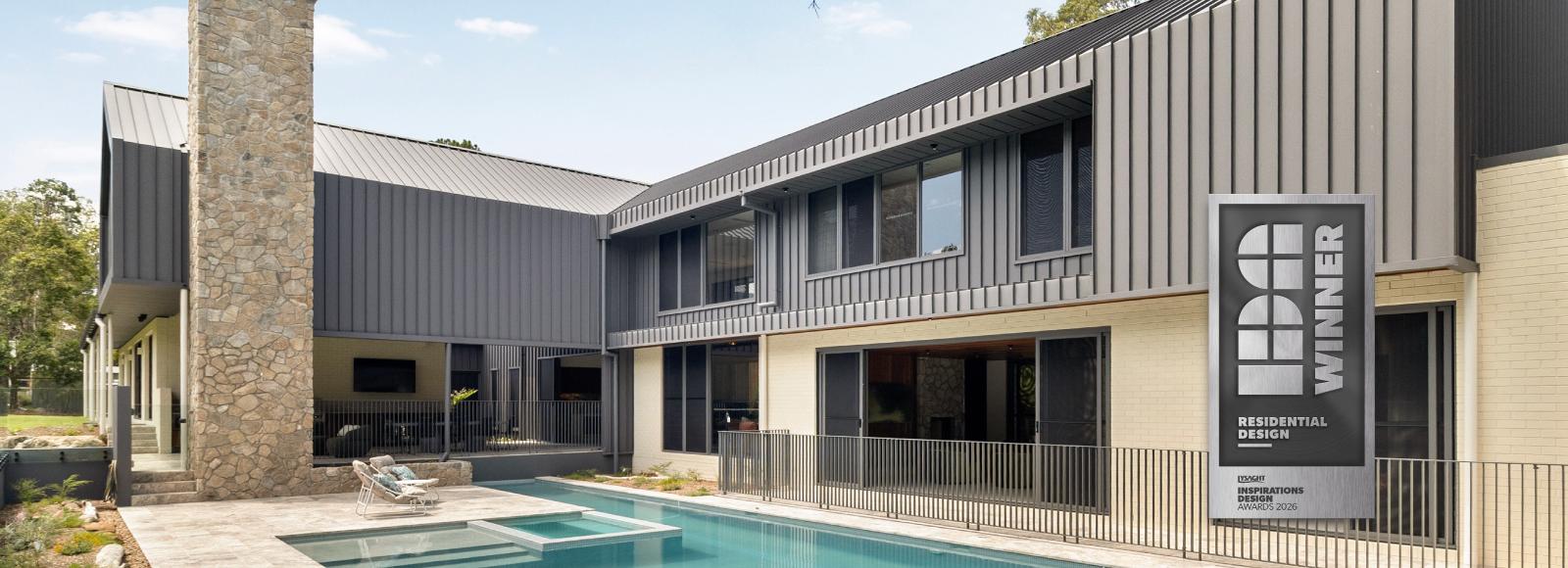MacKenzie House's charcoal-clad rear facade, stone chimney and pool, with a Residential Design Winner badge.