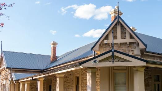 Heritage stone home with CUSTOM ORB® roofing, showcasing a blend of traditional architecture and modern roofing solutions under a sunny sky.