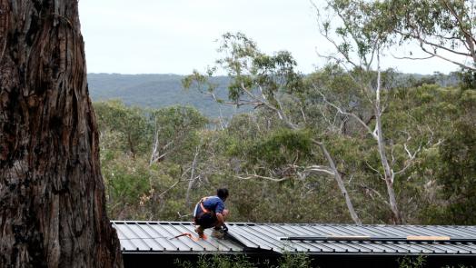 Worker installing steel cyclone roofing on a home in a bushland setting