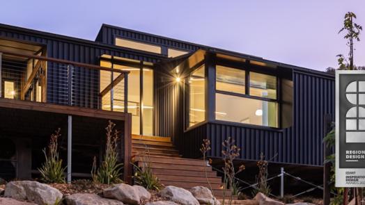 Blackheath Mountain Retreat at dusk, black steel cladding and lit timber decks, with a Regional Design Winner badge.