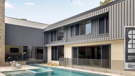 MacKenzie House's charcoal-clad rear facade, stone chimney and pool, with a Residential Design Winner badge.