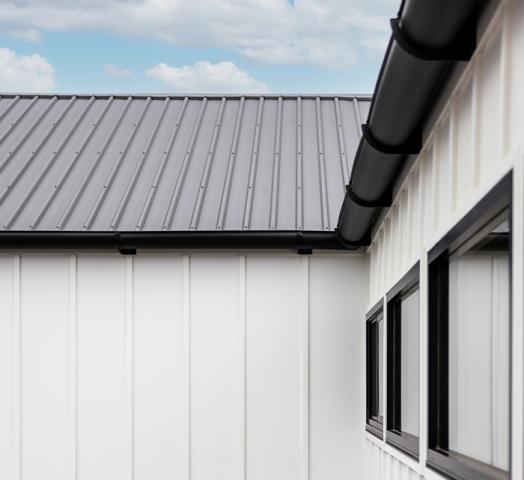 Modern home with black gutters and steel roofing, featuring white panel walls and a seamless gutter system.