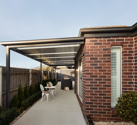 Modern brick home with covered outdoor patio, gable roof carport with polycarbonate panels, and concrete driveway in landscaped backyard