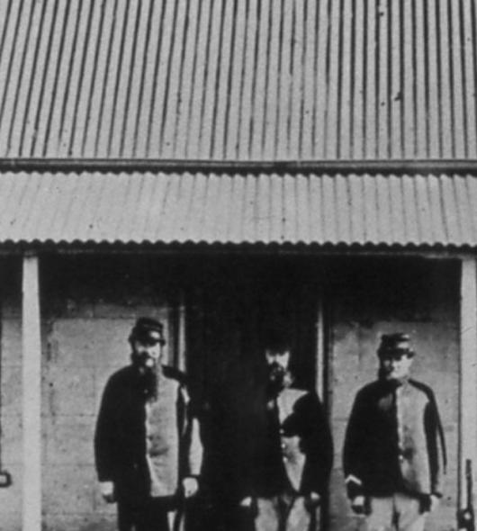 A black and white photo of three men standing on the verandah of a building with an early LYSAGHT® roof