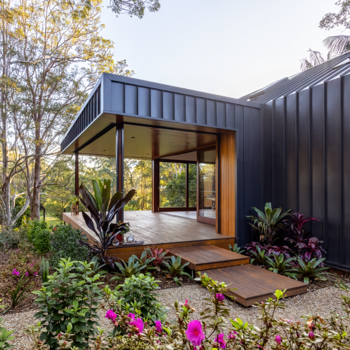 Modern house exterior featuring LYSAGHT® ZENITH® range ENSEAM® cladding in a sleek, dark finish, combined with warm timber paneling and natural stone elements. 