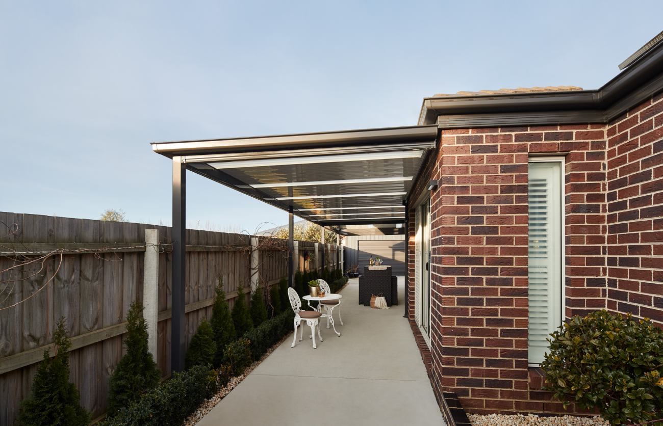 Modern brick home with covered outdoor patio, gable roof carport with polycarbonate panels, and concrete driveway in landscaped backyard