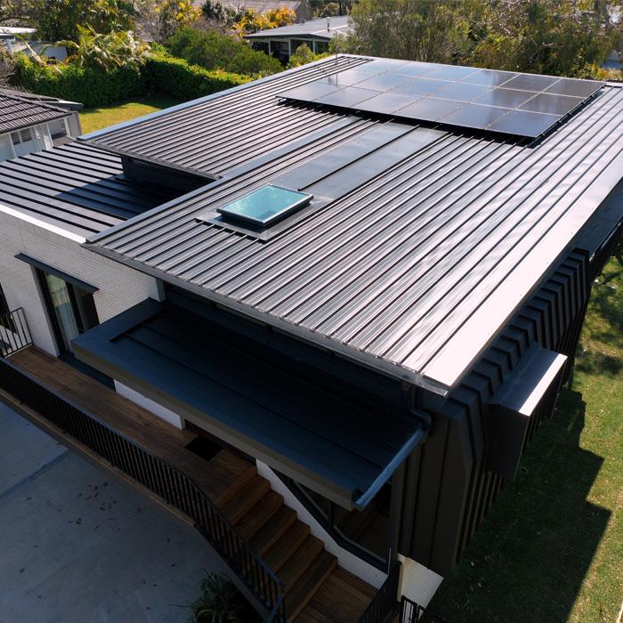 Aerial view of a modern flat-roof home with dark grey Lysaght COLORBOND® roofing sheets and solar panels