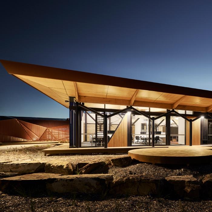 Larnangurrak’s glazed office wing at dusk, with a timber-lined roof, circular deck and boulders