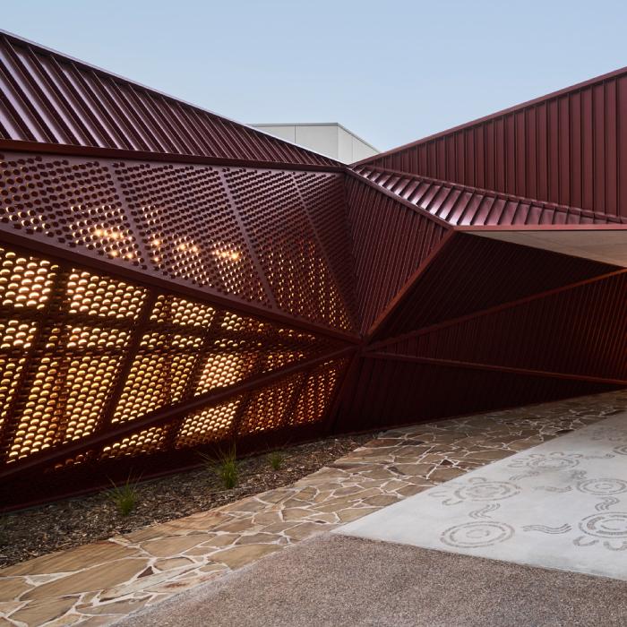 Light shines through angular ochre steel screens beside a path with circular motifs.