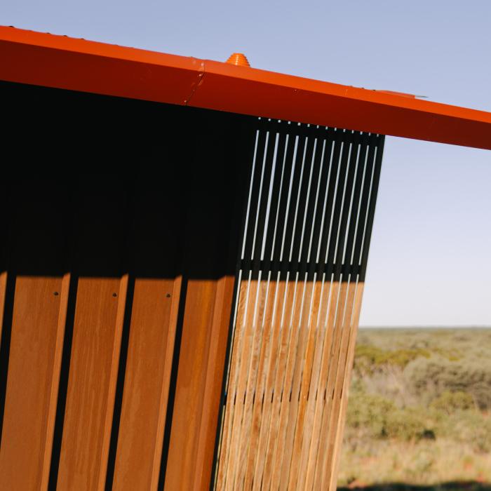 Close-up of a lodge's bright red steel roof edge and timber-batten screen wall