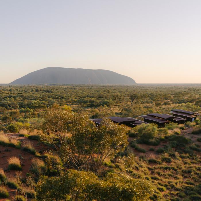Uluru rises on the horizon beyond eco-lodges set in desert scrub at dawn