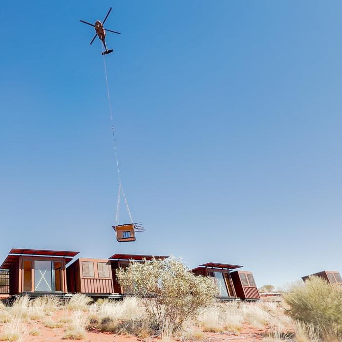 A helicopter airlifts a building module onto eco-lodges on a desert site