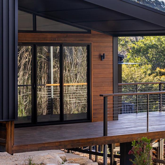 Timber deck with wire balustrade beside sliding glass doors and a timber-clad wall under a raked roof.