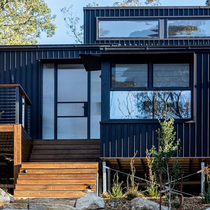Timber stairs rising to the entry, with clerestory windows set into the black vertical steel cladding.