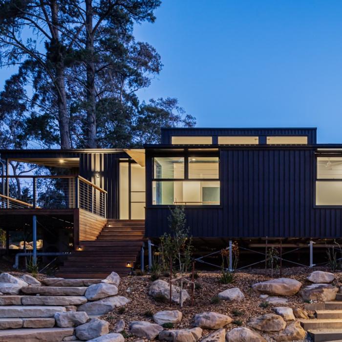 The retreat's front at dusk beneath tall gums, with sandstone boulder steps leading up to the house.