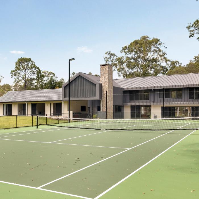  MacKenzie House seen across a tennis court, its long gabled form set against established trees.