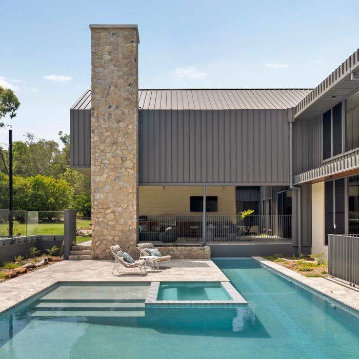 A tall stone chimney beside MacKenzie House's charcoal-clad gable, with a pool and sun loungers below.