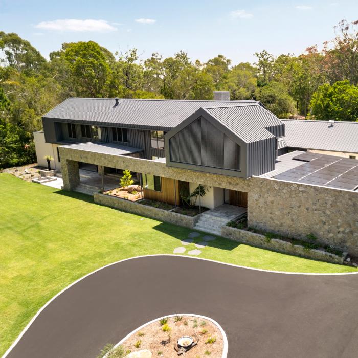 Aerial view of MacKenzie House's front, with dark steel roofs, a stone ground floor and a circular driveway.