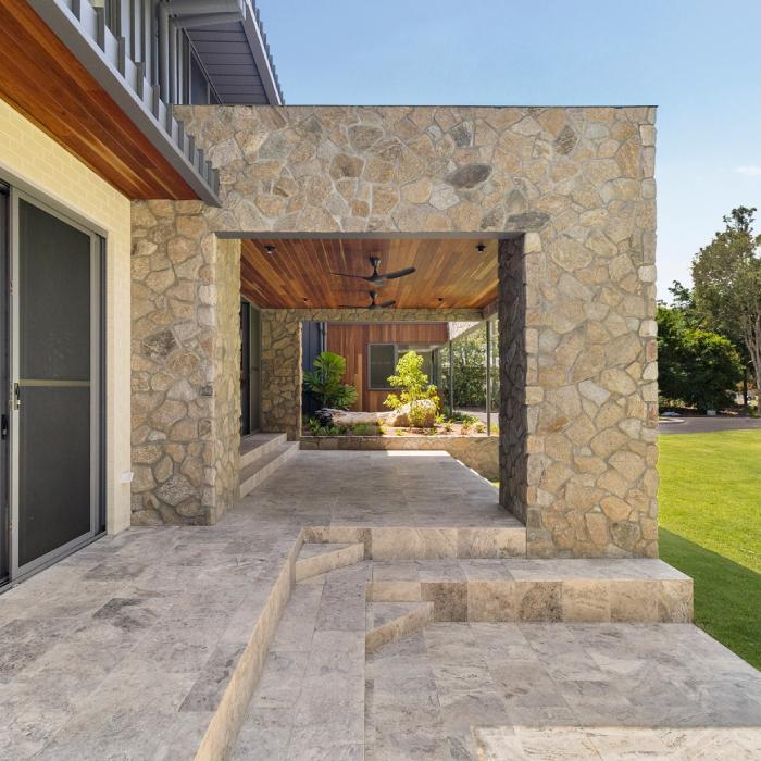 A stone-walled breezeway with a timber-lined ceiling leading to a planted courtyard at MacKenzie House.
