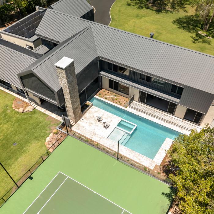 Aerial view of MacKenzie House's rear pool, spa and tennis court beside its charcoal steel roofs.