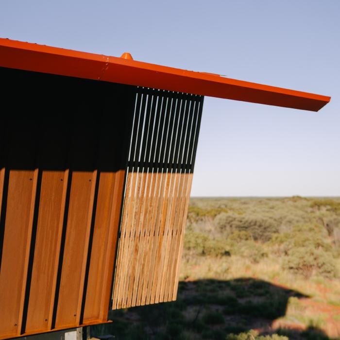 Etna Red roof edge projecting over dark corrugated cladding and timber battens, with desert scrub beyond.