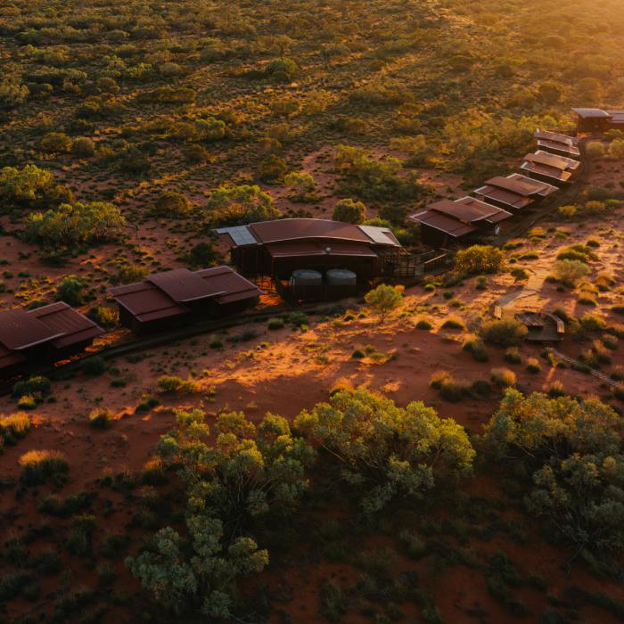 Aerial view at golden hour of low modules linked by a boardwalk along a red sand dune.