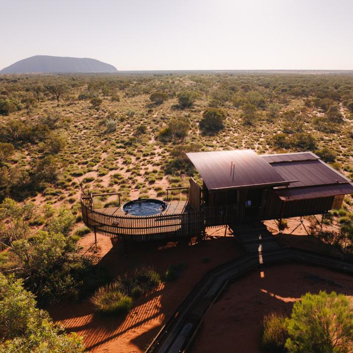 Aerial view of a lodge with a curved deck and round plunge pool, looking out across the desert to Uluru.