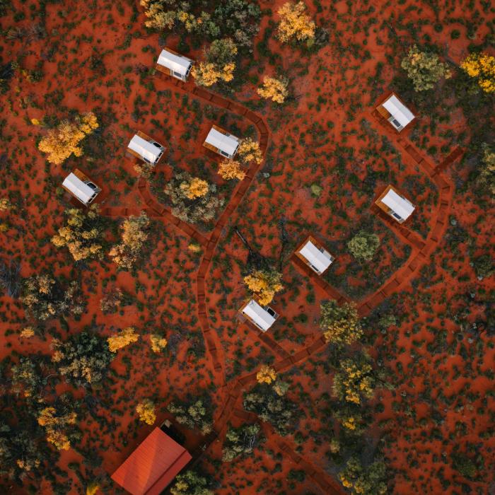 Top-down view of sleeping pods scattered among trees and spinifex, linked by paths in the red sand.