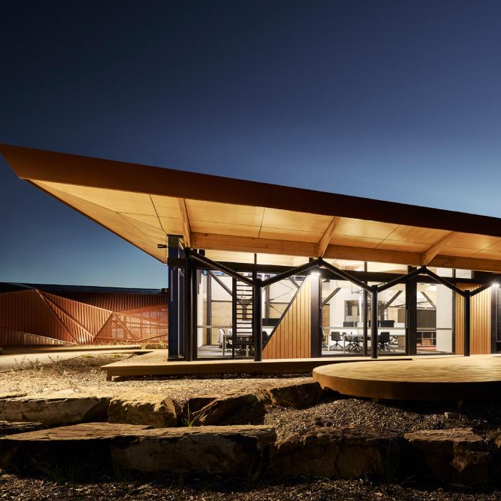 Larnangurrak’s glazed office wing lit at night beneath a broad timber-lined roof.