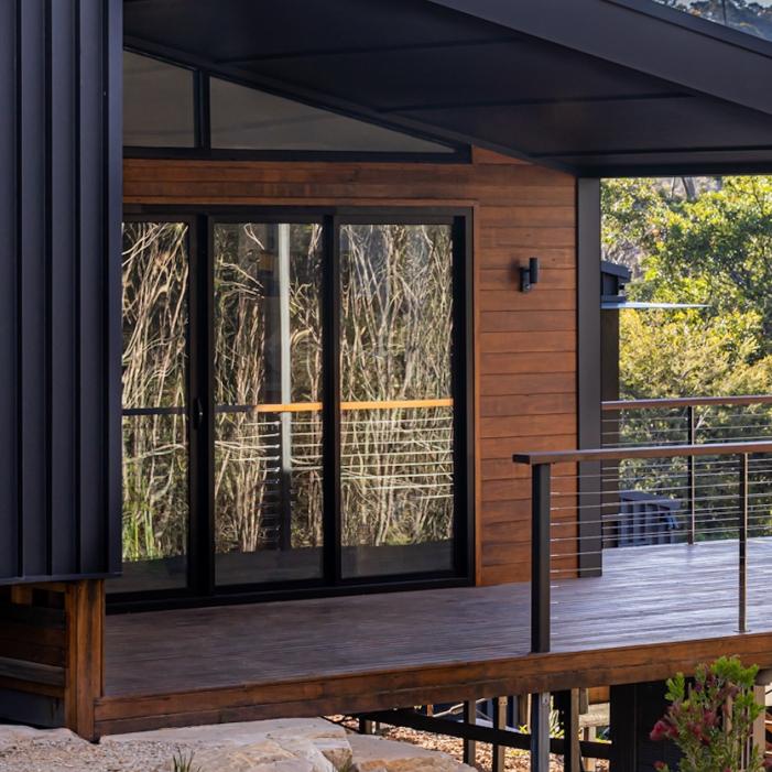 Blackheath Mountain Retreat’s timber deck and glazed doors reflecting trees in daylight.